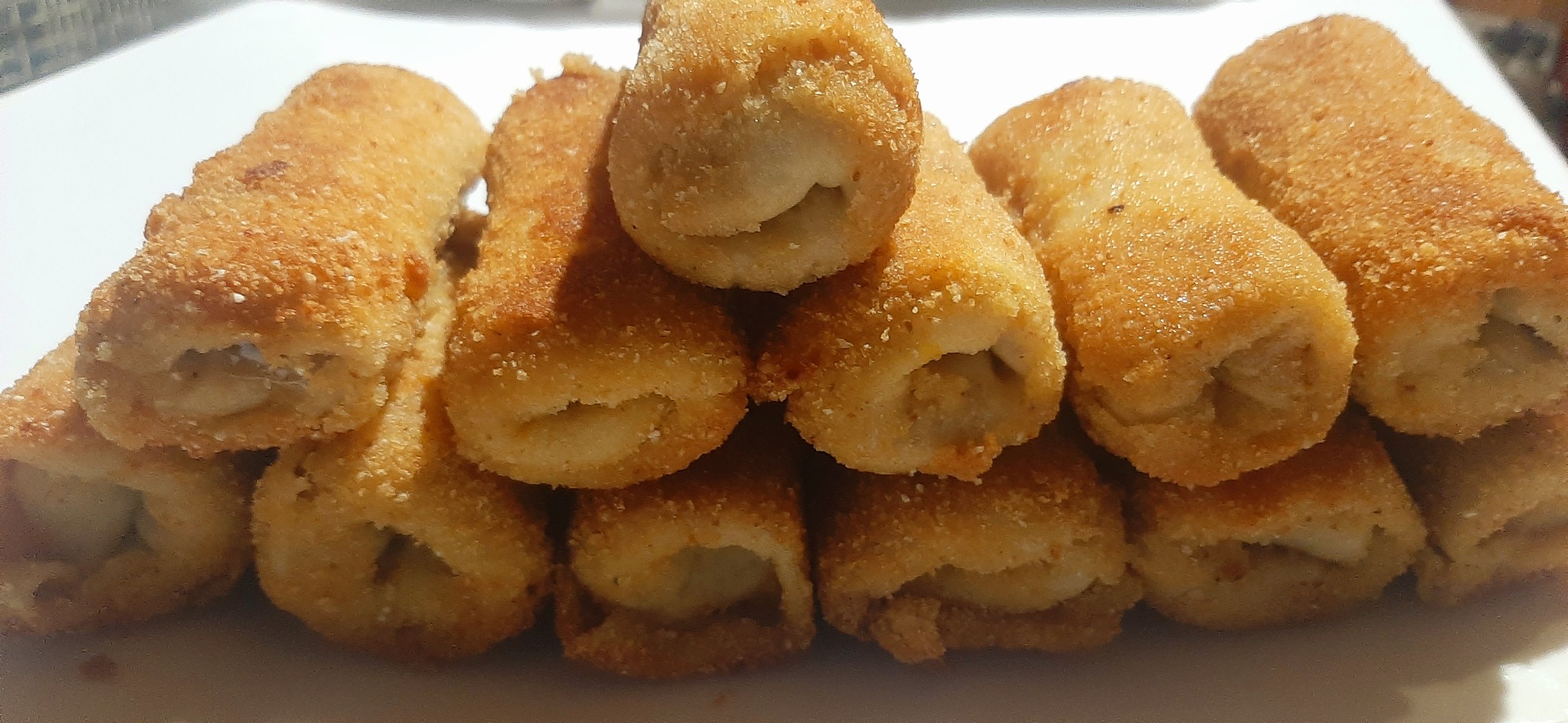 Stos krokietów z kapustą i grzybami na białym talerzu, z widoczną chrupiącą panierką i farszem.