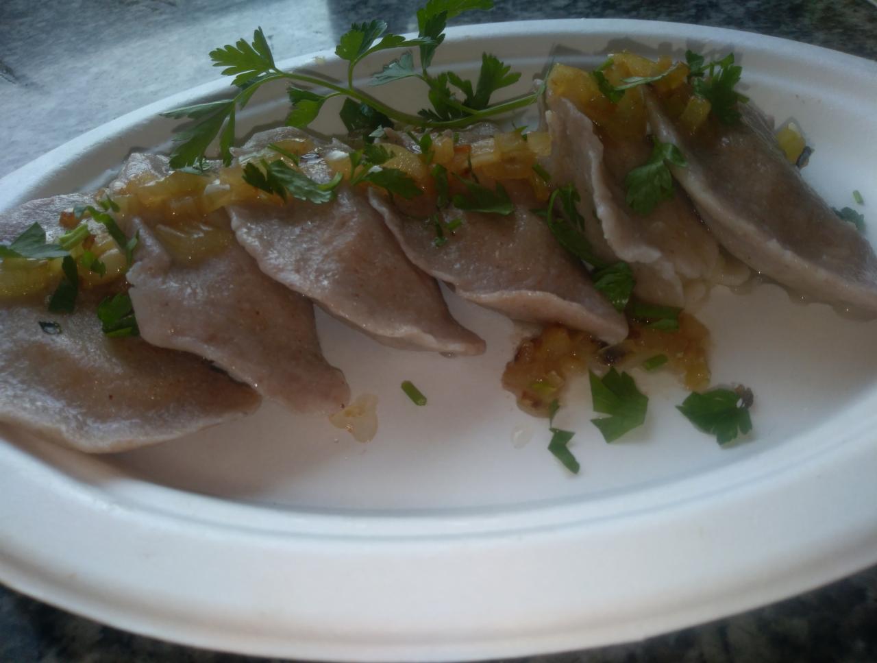 Porcja szarych pierogów okraszonych sosem i posypanych świeżą zieloną pietruszką na białym talerzu.