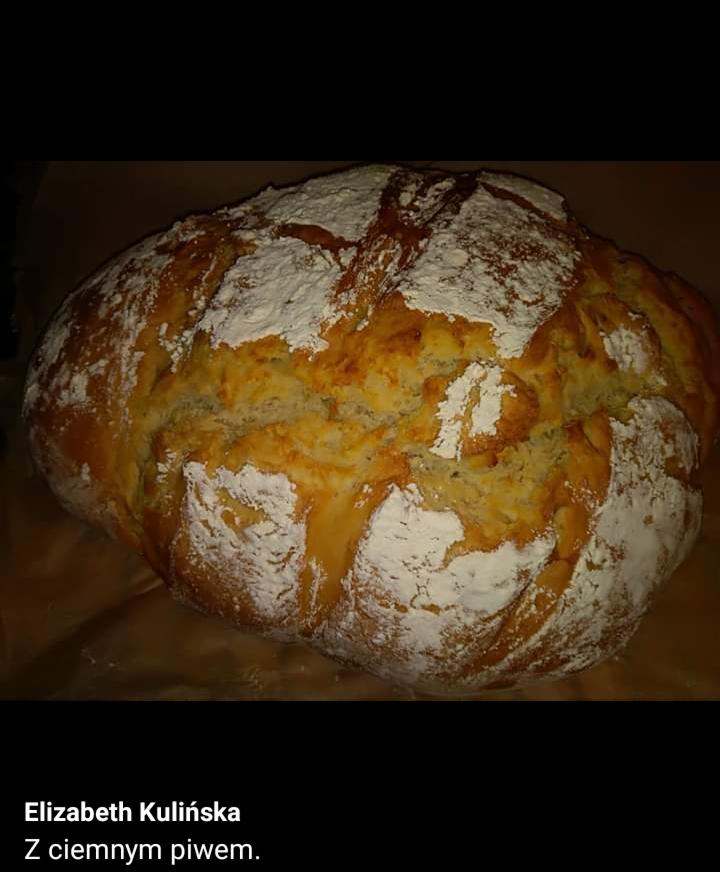 Duży bochen chleba rustykalnego posypany mąką, z widoczną popękaną skórką, na brązowym tle.