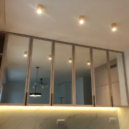 Nowoczesna kuchnia z g&oacute;rnymi szafkami z lustrzanymi frontami, podświetleniem LED pod szafkami i marmurowym blatem.