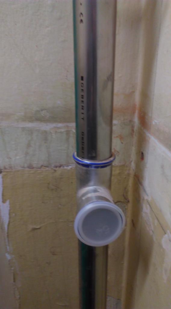 Połączenie rur kanalizacyjnych Geberit z niebieskim pierścieniem uszczelniającym, widoczne na tle ściany w trakcie remontu w Warszawie.
