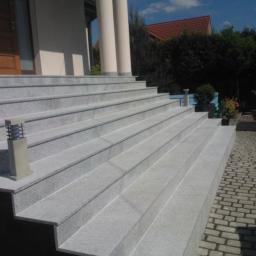 Bianko-Bud - Granitowe schody wejściowe do domu z kolumnami, oświetlone lampami, prowadzące do drewnianych drzwi.