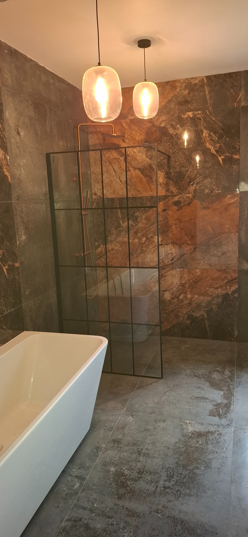 Nowoczesna łazienka z kabiną prysznicową typu walk-in, marmurowymi płytkami i wiszącymi lampami. Minimalistyczna wanna i miedziana armatura.