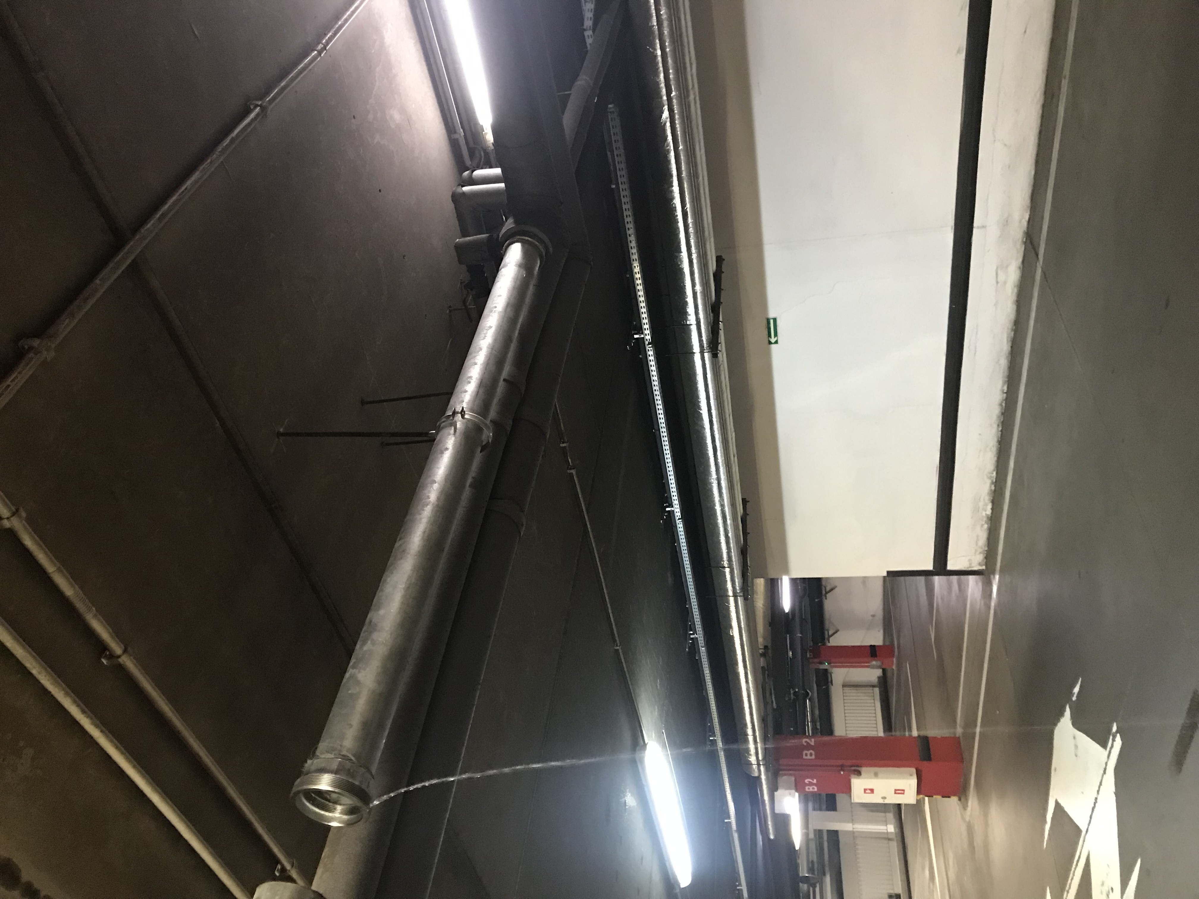 Wyciek wody z metalowej rury instalacji hydraulicznej zamontowanej pod sufitem parkingu podziemnego.