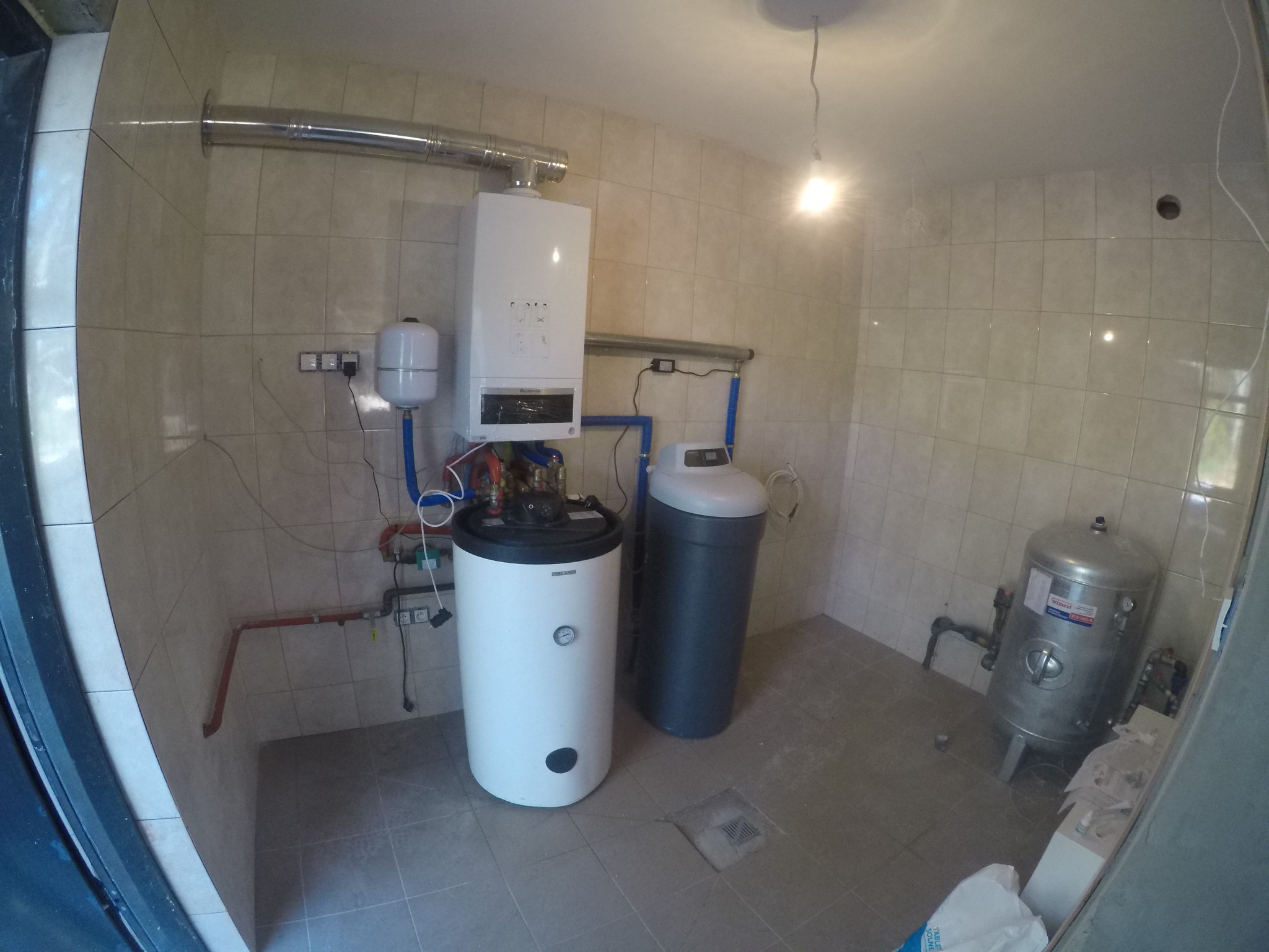 Instalacja kotła gazowego, zbiornika buforowego, zmiękczacza wody i naczynia przeponowego w kotłowni wyłożonej płytkami ceramicznymi.
