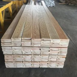 Stos ułożonych desek z pióro-wpustem, przygotowanych do montażu, z widocznym usłojeniem drewna i obróbką krawędzi, w tle maszyny stolarskie.