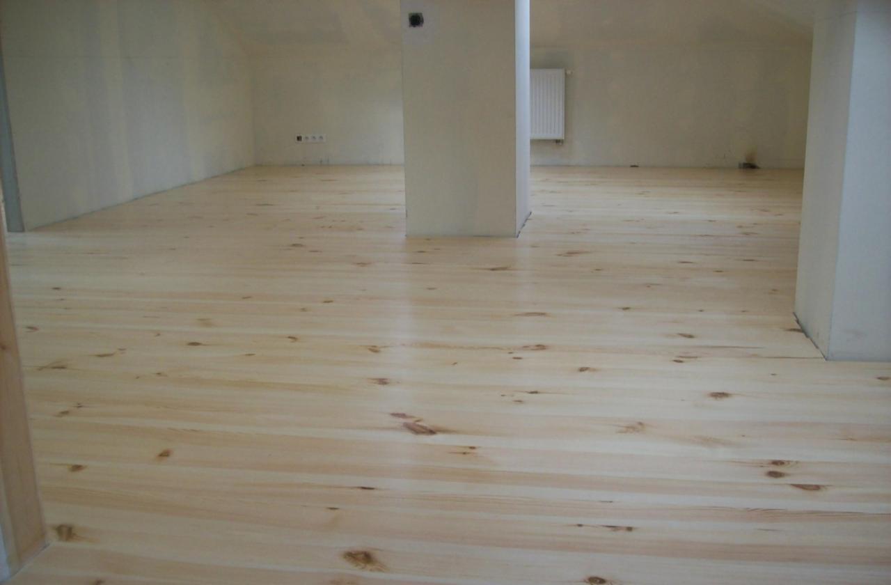 Jasna, świeżo położona podłoga z desek w pokoju na poddaszu, widoczne sęki i słojowanie drewna, z kolumną konstrukcyjną w tle.