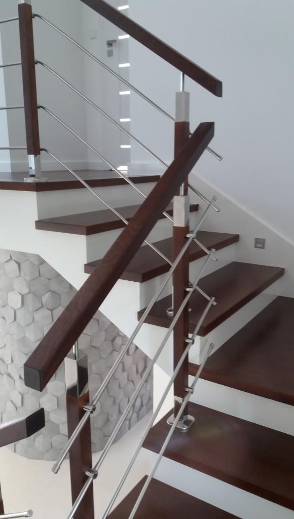 Nowoczesne schody z ciemnego drewna i metalowymi balustradami, widok z dołu, dekoracyjna ściana w tle.