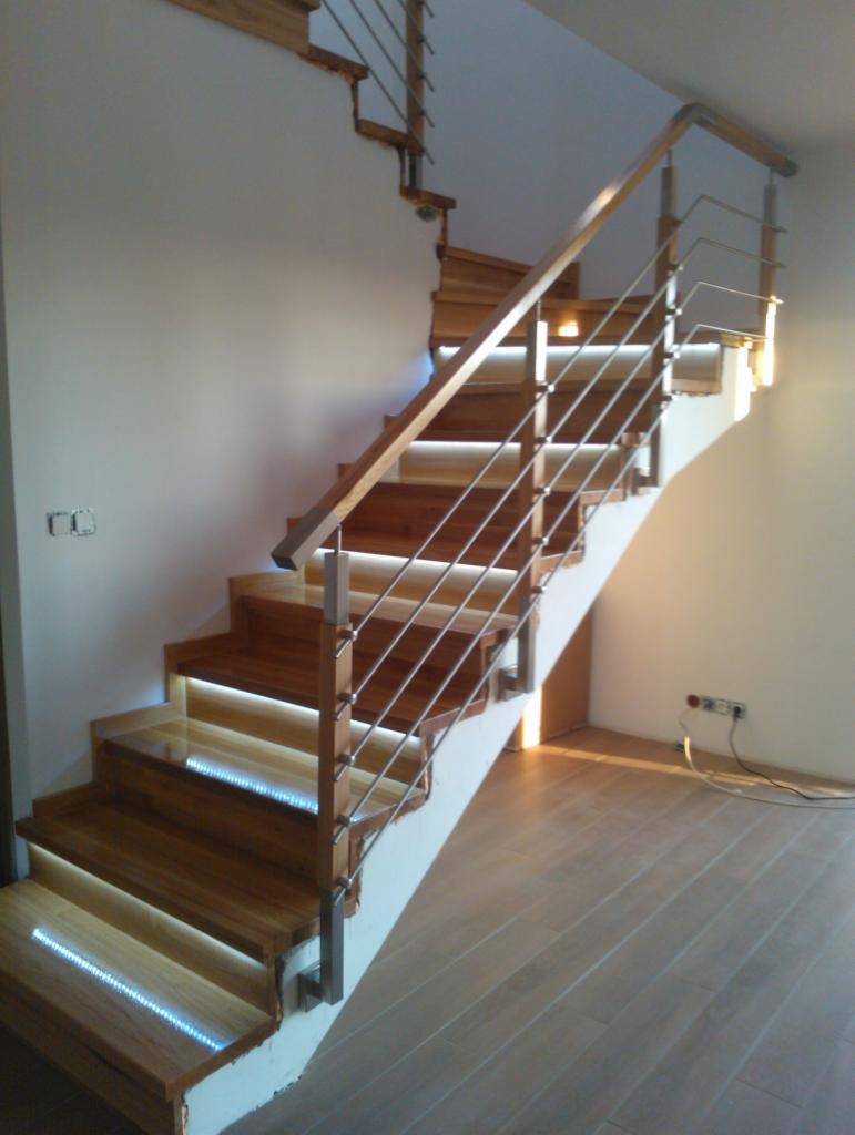 Drewniane schody z metalową balustradą, podświetlone diodami LED na każdym stopniu, w jasnym wnętrzu z panelami podłogowymi.