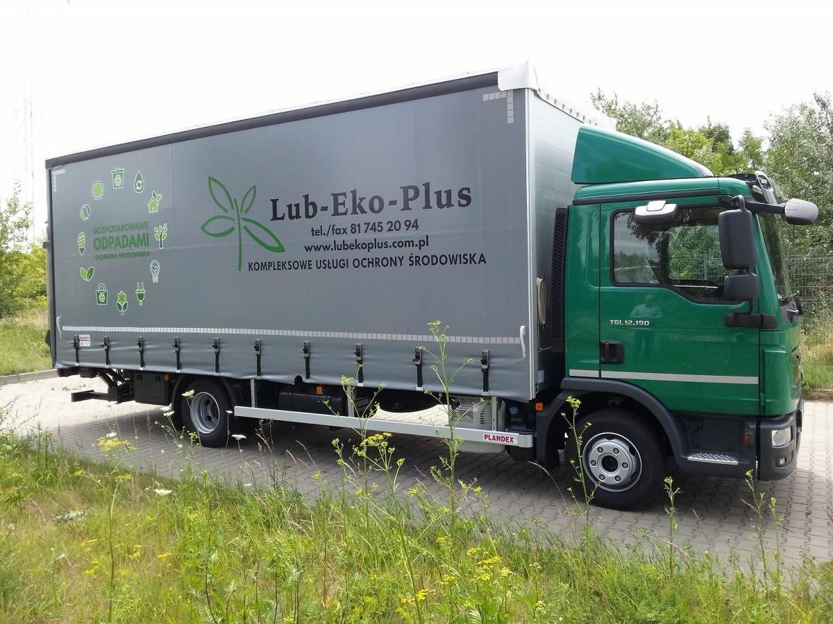 Zielona ciężarówka MAN TGL 12.190 z szarą naczepą z logo firmy Lub-Eko-Plus i napisami 'Gospodarowanie odpadami' oraz 'Kompleksowe usługi ochrony środowiska', zaparkowana na kostce brukowej, widok...