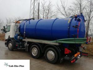 Ciężarówka asenizacyjna w kolorze biało-niebieskim z dużym zbiornikiem, widoczna z boku, z zielonymi wężami na platformie. Na dole widoczne logo firmy Lab-Eko-Plus.