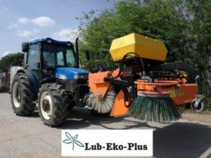 Niebieski traktor z zamontowaną pomarańczową szczotką do czyszczenia dróg i żółtym zbiornikiem na zanieczyszczenia, widoczne drzewa w tle, na dole logo firmy Lub-Eko-Plus.