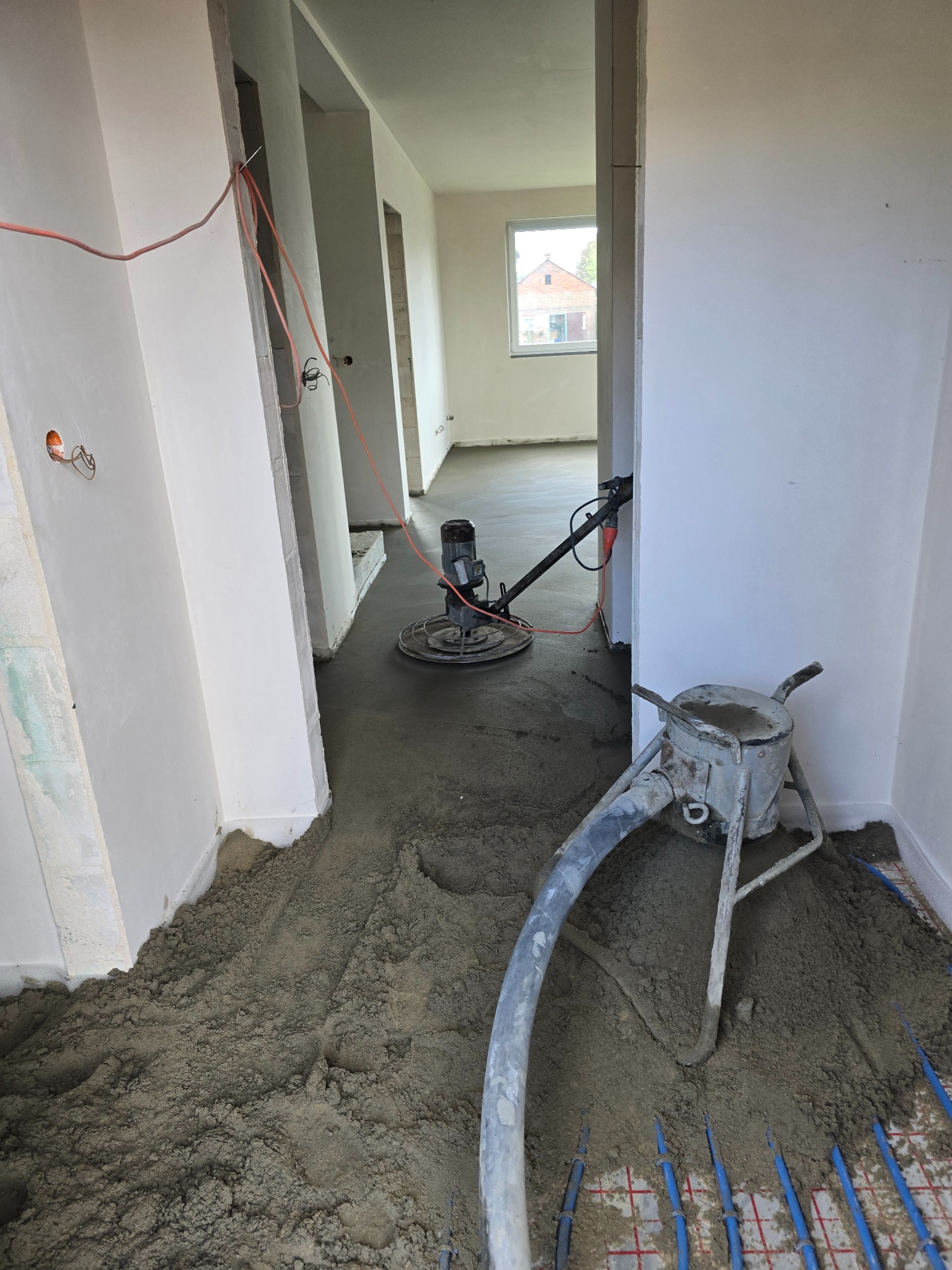 Aplikacja jastrychu na ogrzewanie podłogowe. Widoczna maszyna do rozprowadzania i zacierania. Świeża wylewka w jasnym wnętrzu z instalacjami.