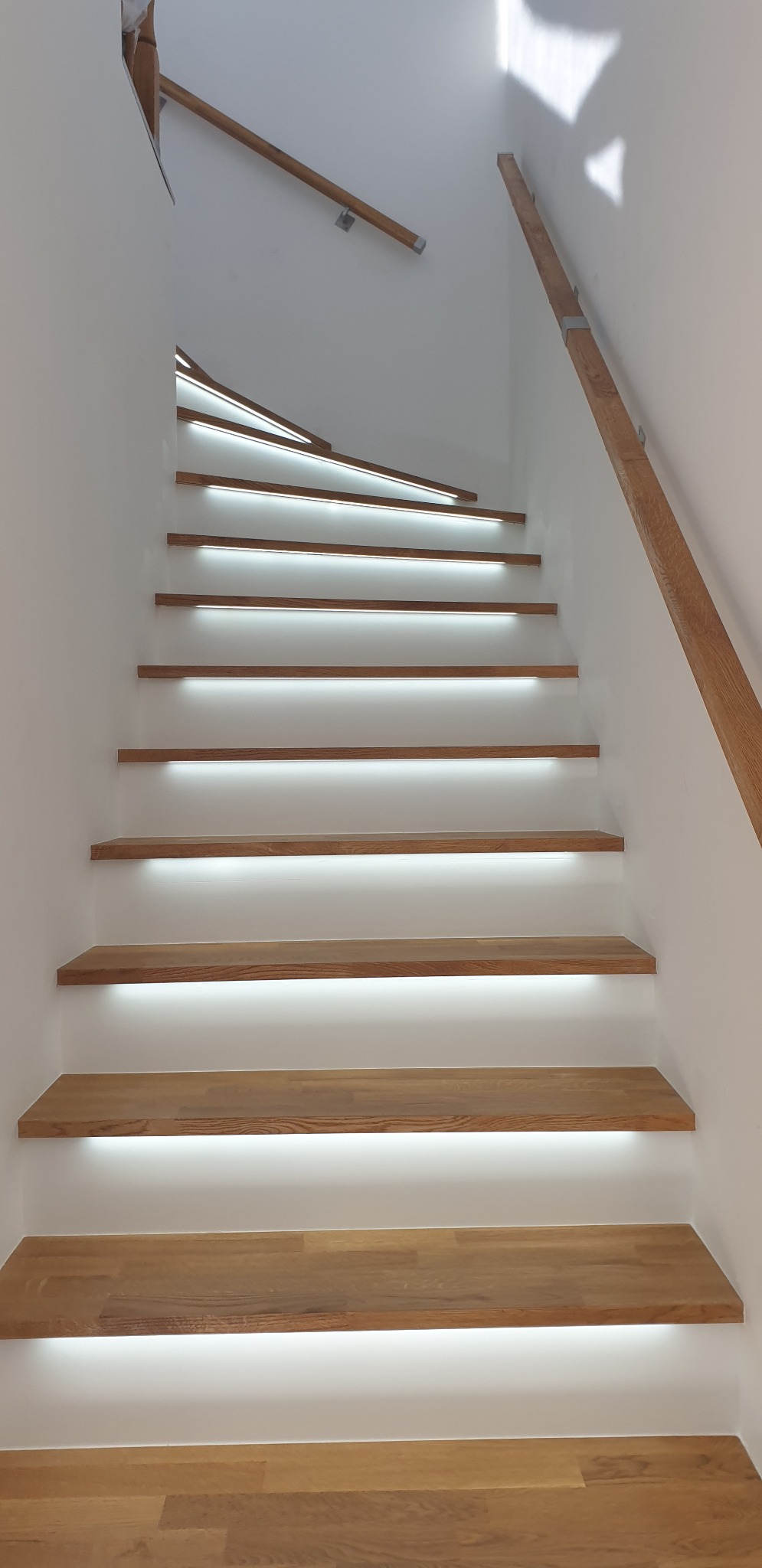 Nowoczesne schody drewniane z podświetleniem LED, widok z dołu, jasne wnętrze.