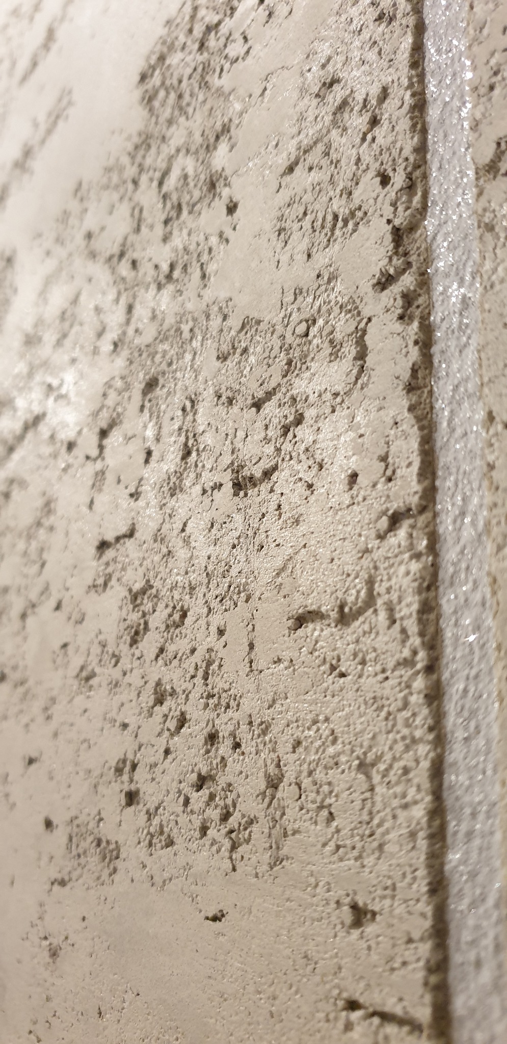 Szorstka, beżowa ściana z efektem dekoracyjnym, zabezpieczona taśmą malarską przy krawędzi.