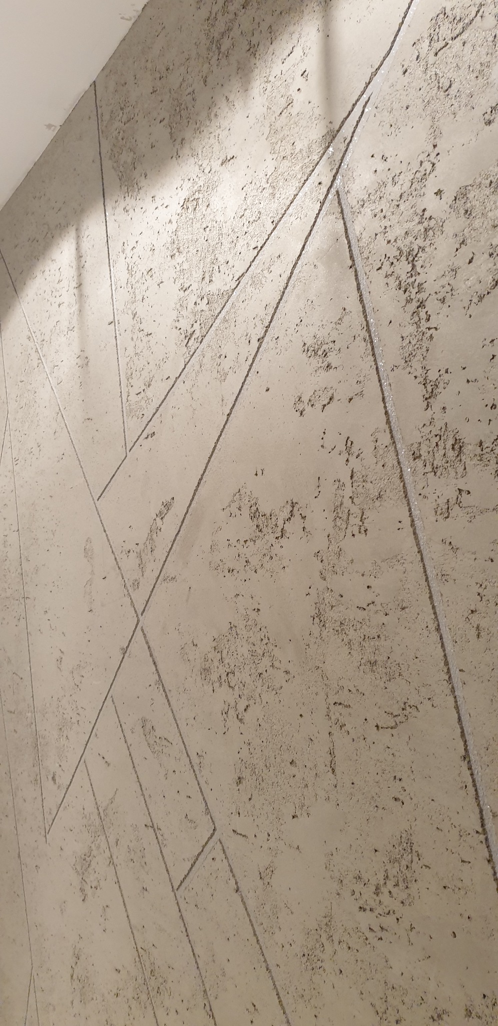 Dekoracyjna ściana z beżową, chropowatą fakturą i geometrycznym wzorem z delikatnych, srebrnych linii.