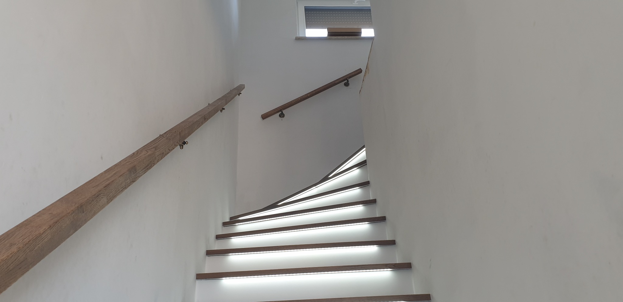 Nowoczesne schody z podświetleniem LED na stopniach i drewnianymi poręczami, widok z dołu.