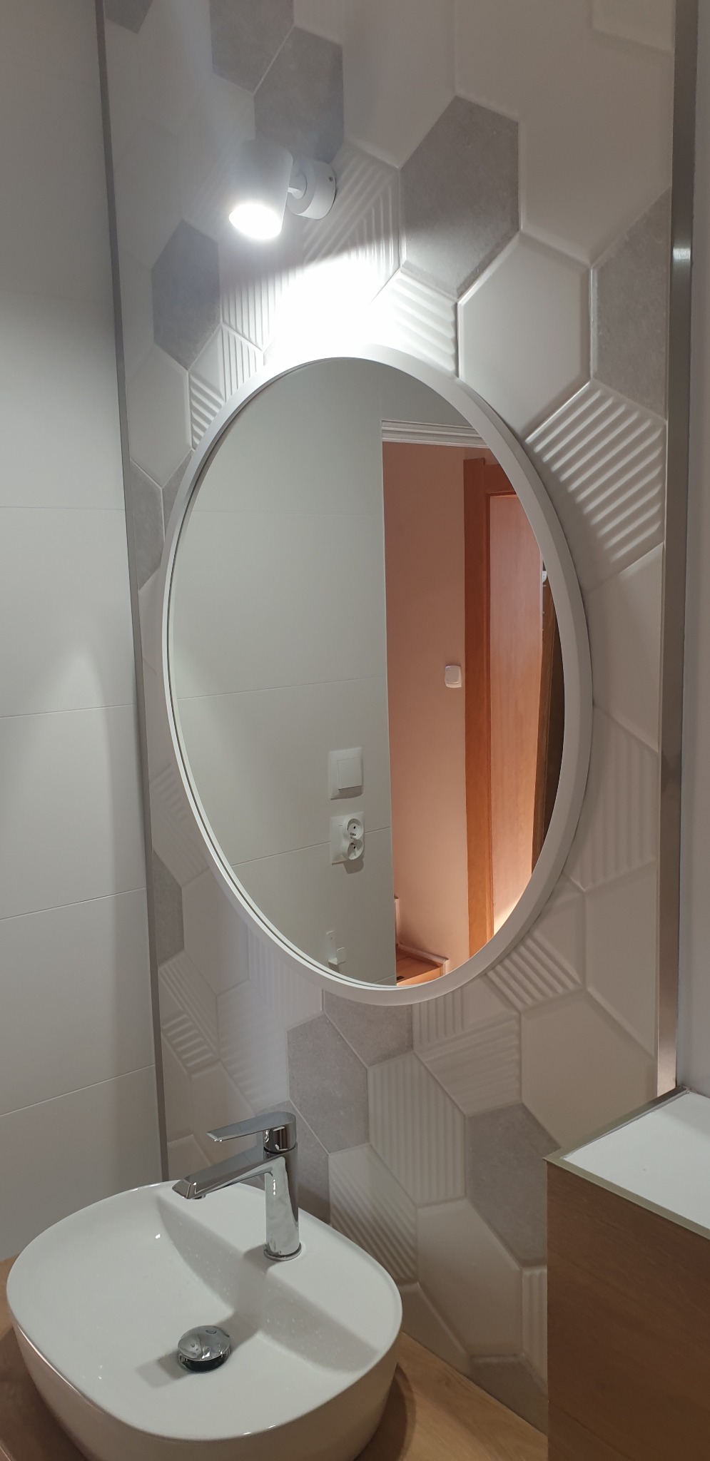 Nowoczesna łazienka z umywalką nablatową, okrągłym lustrem podświetlonym od tyłu i heksagonalnymi płytkami w odcieniach szarości i bieli