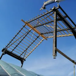 Montaż drewnianej konstrukcji dachu z użyciem dźwigu CKD na tle błękitnego nieba, widoczna folia zabezpieczająca poniżej.