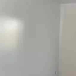 Świeżo pomalowane na biało ściany w rogu pokoju, widoczny fragment podłogi i gniazdko elektryczne.