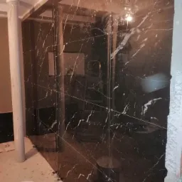 Ściana wyłożona czarnymi płytkami imitującymi marmur z białymi żyłami, widoczne krzyżyki dystansowe i wiadro z klejem na podłodze w trakcie prac glazurniczych.