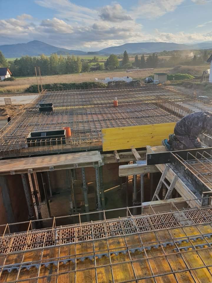 Zbrojenie stropu na budowie domu jednorodzinnego, widoczne szalunki, stalowe pręty i elementy konstrukcyjne, w tle krajobraz z polami i górami.