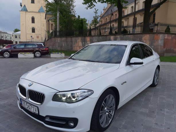 Białe BMW serii 5 na tle miejskiego krajobrazu z budynkiem w tle.