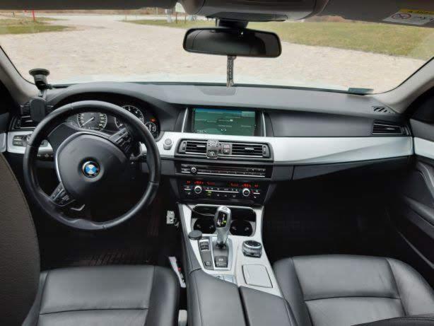 Wnętrze samochodu marki BMW z czarną skórzaną tapicerką, widok na deskę rozdzielczą, kierownicę z logo i automatyczną skrzynię biegów.