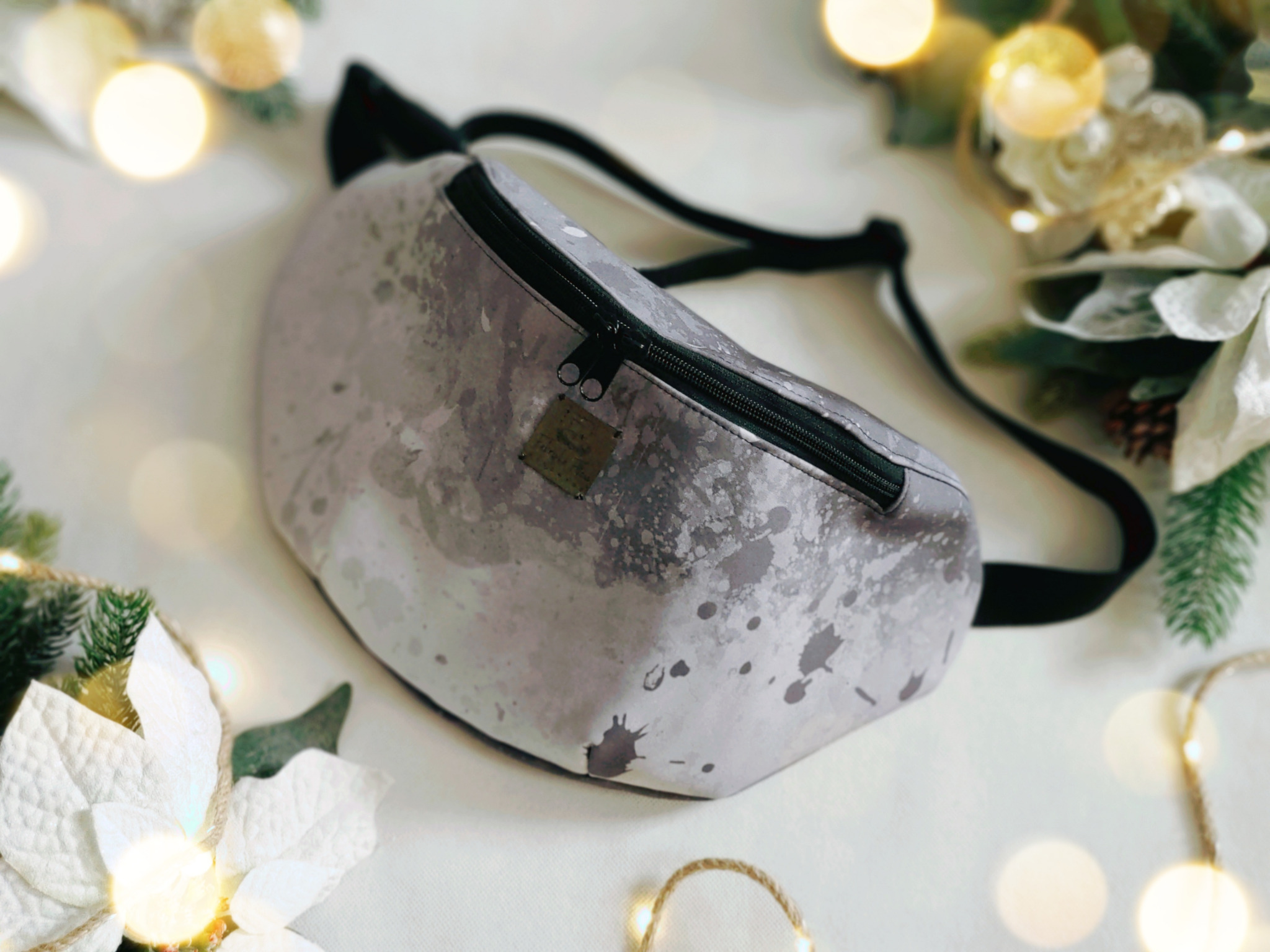 Szara nerka biodrowa z efektem plam, leżąca na białym tle z dekoracjami świątecznymi i delikatnym oświetleniem.