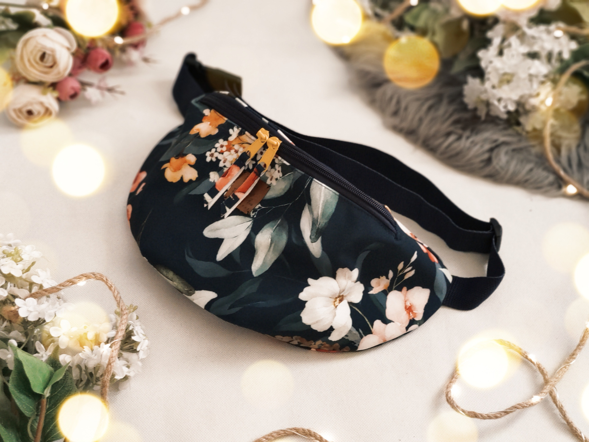 Stylowa nerka z ciemnym, kwiatowym wzorem, leżąca na białym tle z dekoracjami kwiatowymi i delikatnymi światełkami.