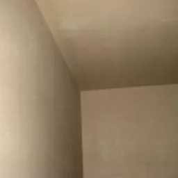 Gładka, beżowa powierzchnia ściany i sufitu po nałożeniu tynku maszynowego, widoczne łączenie pod kątem prostym.