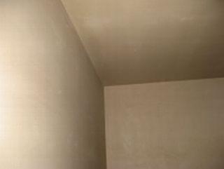 Gładka, beżowa powierzchnia ściany i sufitu po nałożeniu tynku maszynowego, widoczne łączenie pod kątem prostym.