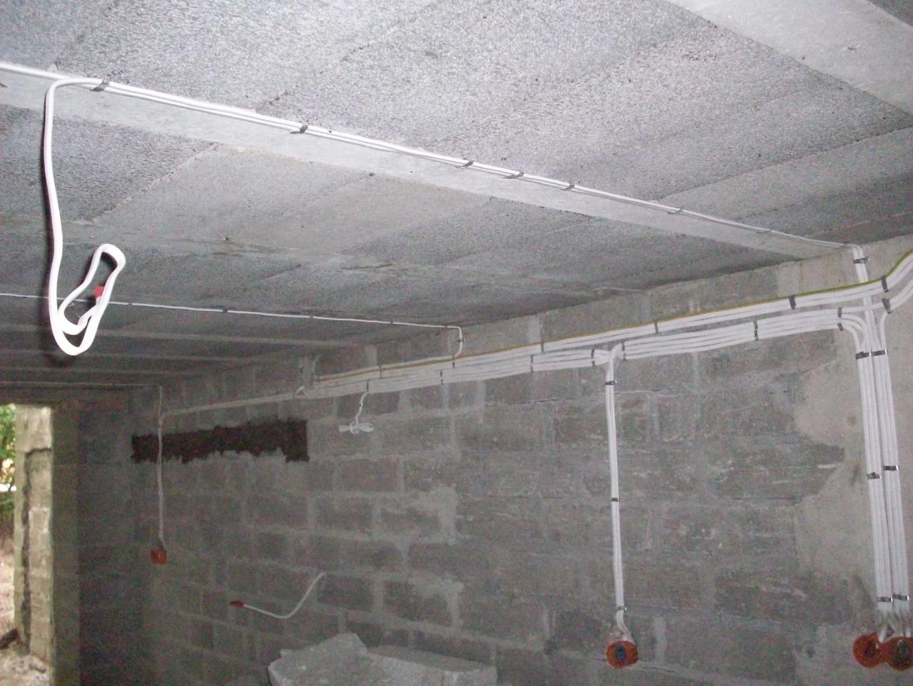 Surowy betonowy strop i ściany z widocznymi przewodami elektrycznymi zamocowanymi uchwytami, instalacja w trakcie realizacji, widoczne puszki pod gniazdka.