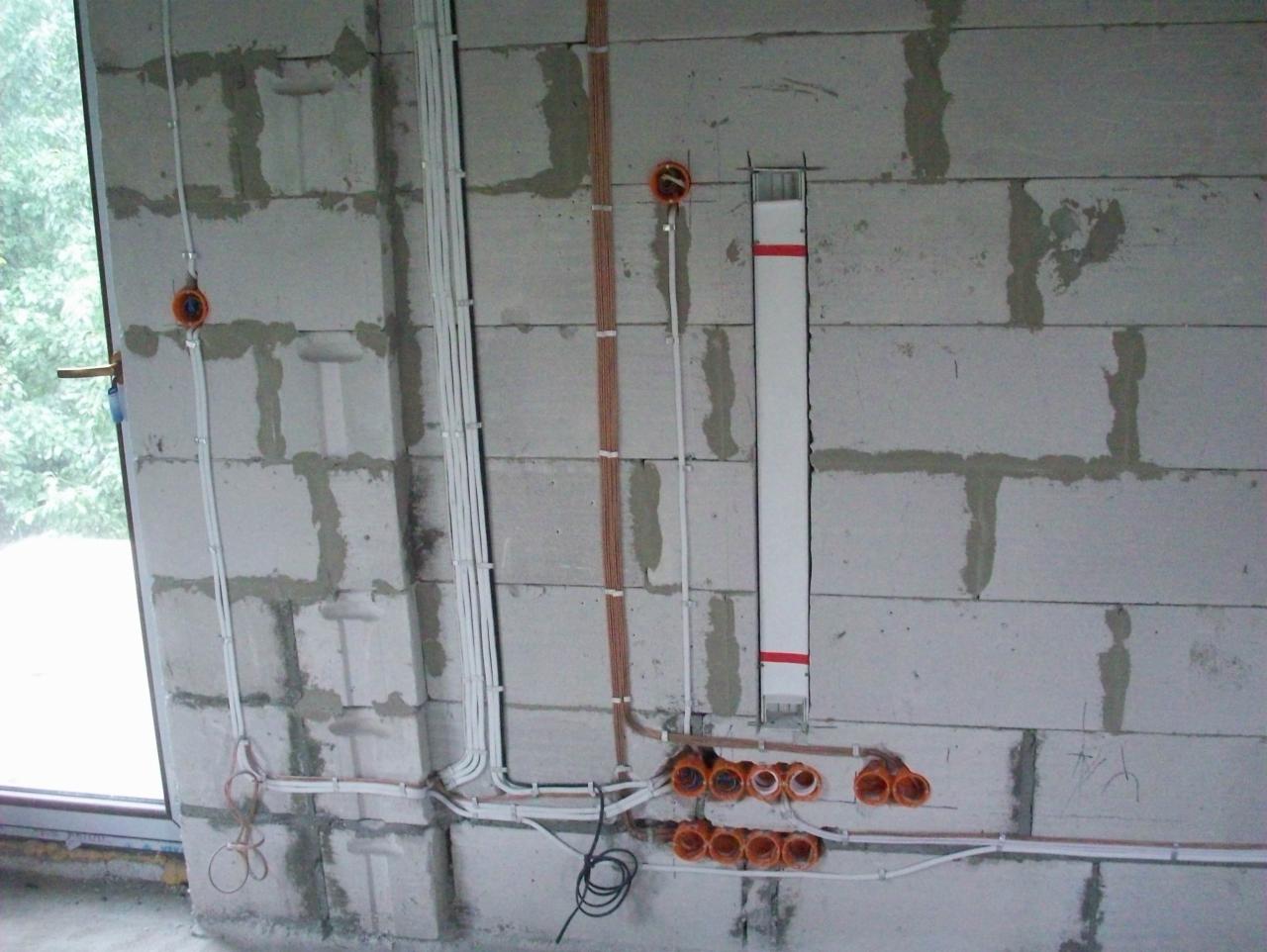 Surowa ściana z betonu komórkowego z widocznymi przewodami elektrycznymi w peszlach i puszkach instalacyjnych, częściowo zamontowanymi, w trakcie prac wykończeniowych.