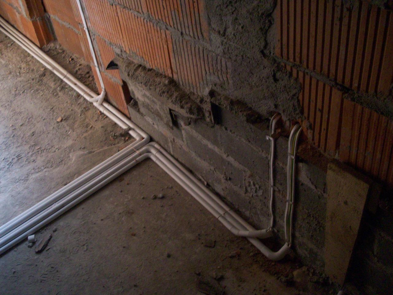 Wewnętrzna instalacja elektryczna w rurkach PCV, prowadzone wzdłuż ceglanej ściany, w surowym stanie, z widocznymi bruzdami i fragmentami betonu.