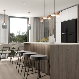 Moma Design Magdalena Moraczyńska - Nowoczesna kuchnia z wyspą, drewnianym wykończeniem, szarymi stołkami barowymi, czarną lodówką Samsung i wiszącymi lampami z miedzianymi akcentami nad wyspą oraz jadalnią z widokiem na zieleń za...