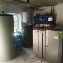 Kotłownia z kotłem Bio Pellmax, zbiornikiem buforowym, zasobnikiem CWU i rozdzielaczem, instalacja w piwnicy z oknem.