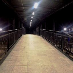 ZRM LEDZIŃSCY SPÓŁKA JAWNA TOMASZ LEDZIŃSKI AGNIESZKA HOFMAN - Zadaszone przejście dla pieszych nad torami kolejowymi, oświetlone rzędem lamp, z metalową konstrukcją i wyłożone płytkami chodnikowymi.