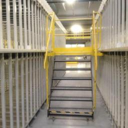 ZRM LEDZIŃSCY SPÓŁKA JAWNA TOMASZ LEDZIŃSKI AGNIESZKA HOFMAN - Wnętrze hali magazynowej z regałami paletowymi i schodami dostępowymi w kolorze żółtym.