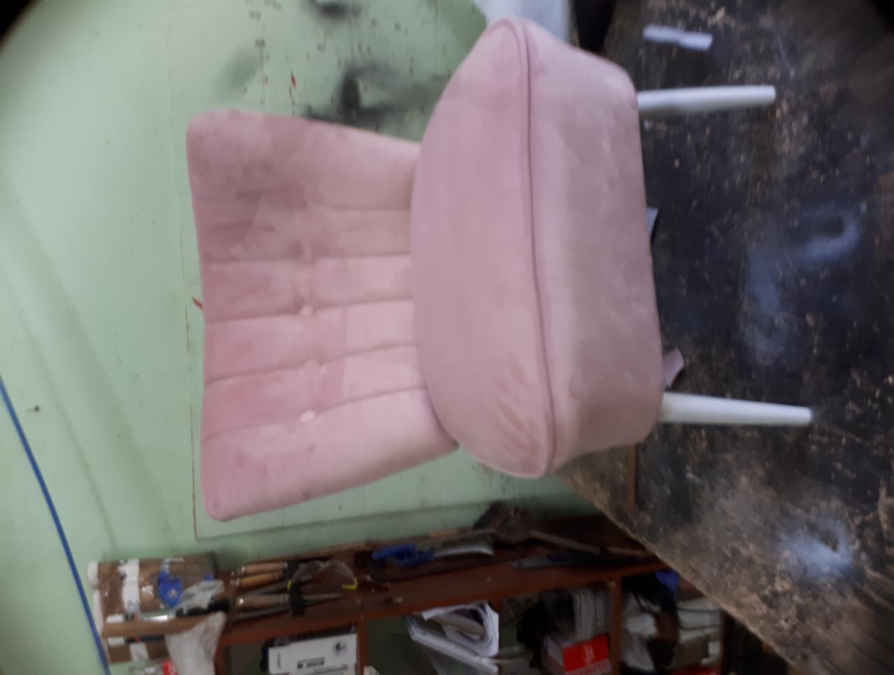 Różowe krzesło z welurowym obiciem i białymi nogami, widoczne w warsztacie z narzędziami na półce w tle.