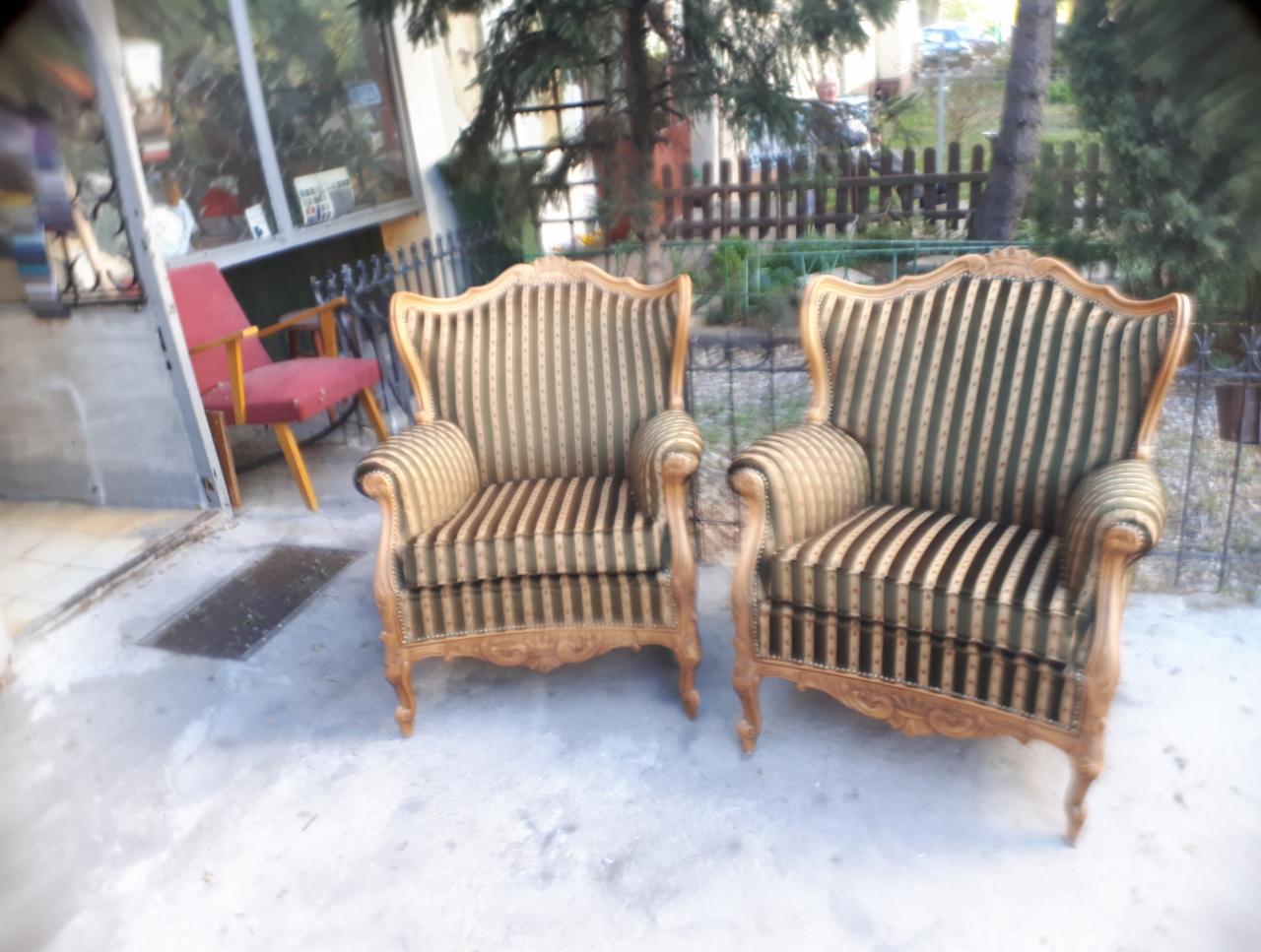 Dwa odnowione fotele w stylu Ludwika Filipa z beżowo-zieloną tapicerką w paski, ustawione na betonowym podłożu przed budynkiem z widocznym oknem i zielenią w tle.