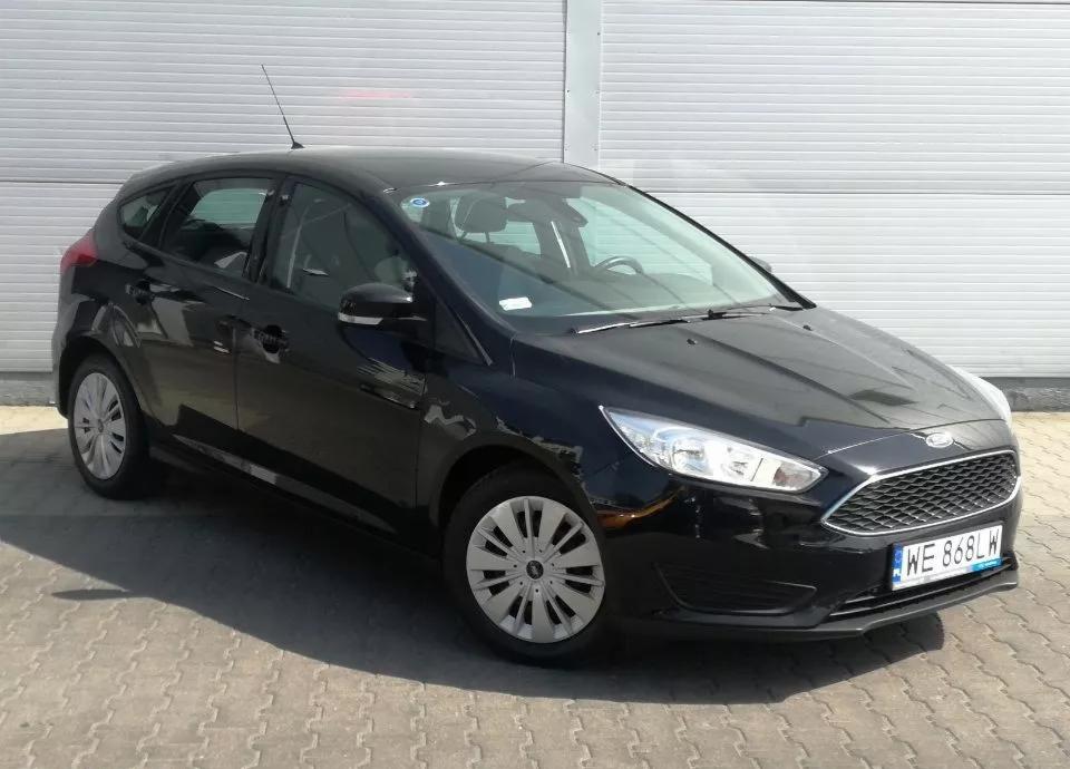 Czarny Ford Focus hatchback zaparkowany na kostce brukowej przed budynkiem z szarej blachy falistej.