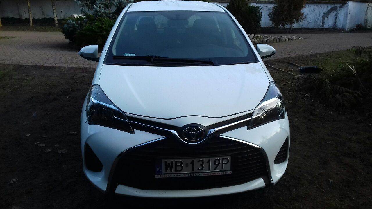Biała Toyota Yaris zaparkowana na ziemi, widok z przodu, z widoczną tablicą rejestracyjną WB 1319P i logo Toyota.