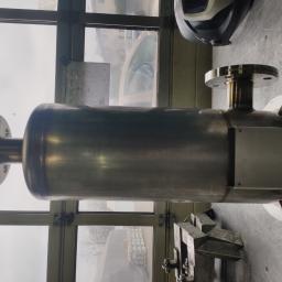 Usługi spawania - Metalowy zbiornik z przyspawanymi kołnierzami, leżący na stole warsztatowym w hali, widoczna maska spawalnicza w tle.