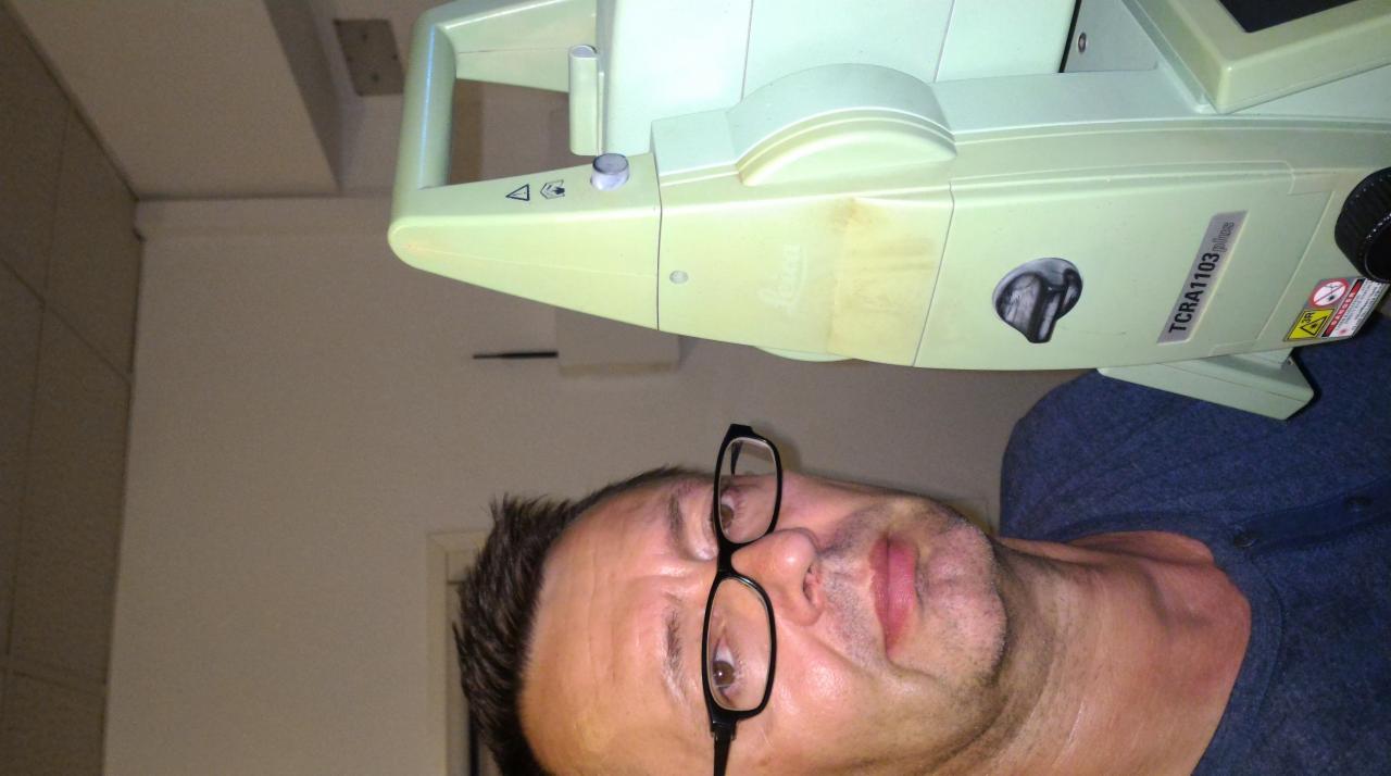 Mężczyzna w okularach pozuje z tachimetrem Leica TCRA1103 plus w pomieszczeniu.