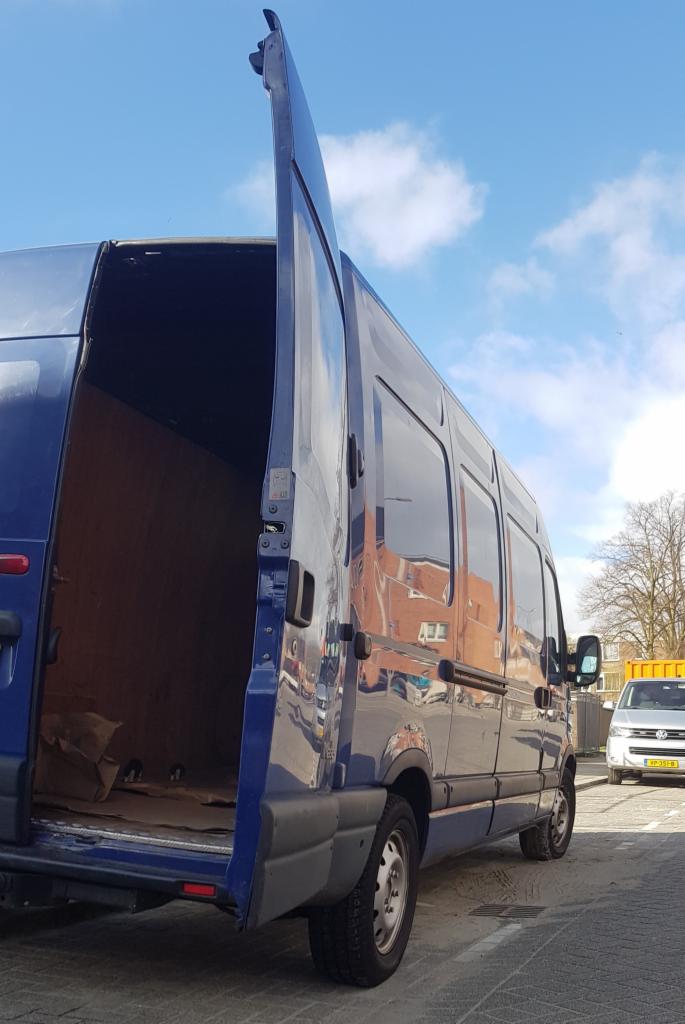 Niebieski bus dostawczy z otwartymi tylnymi drzwiami, wnętrze częściowo załadowane kartonami, widok z boku na tle miejskiej ulicy.