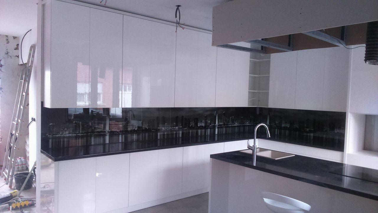 Biała, lakierowana zabudowa kuchenna z czarnym blatem i panelem z motywem panoramy miasta, widoczny fragment instalacji sufitowej i drabina malarska.
