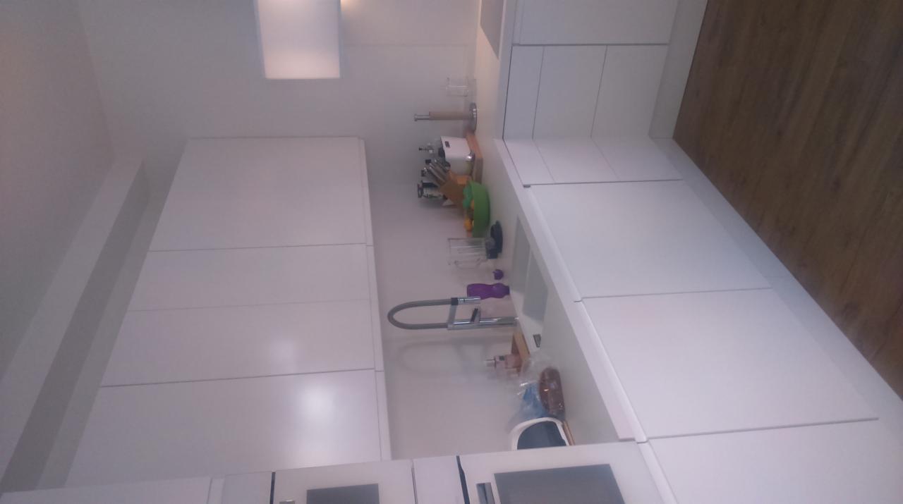 Biała, minimalistyczna zabudowa kuchenna z widocznym zlewem i baterią, na blacie kuchennym akcesoria kuchenne i przybory.