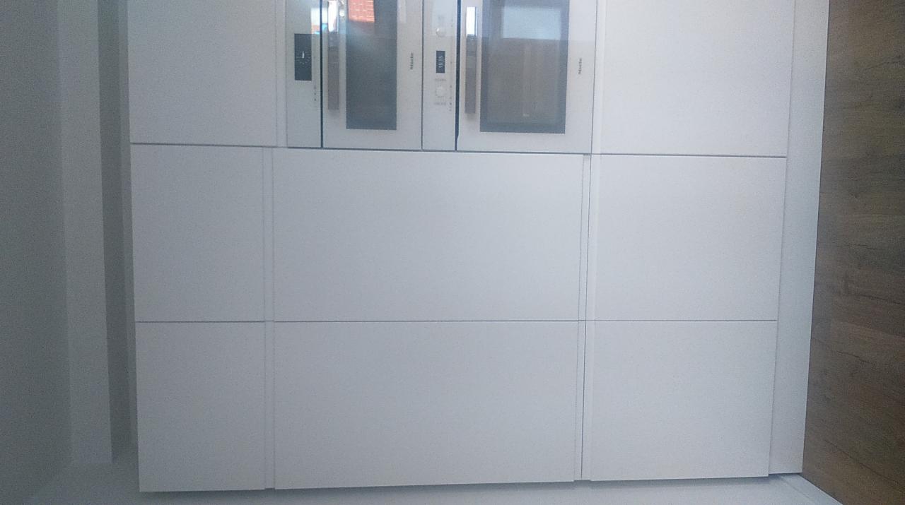 Biała zabudowa kuchenna z wbudowanymi piekarnikami Miele, minimalistyczny design, gładkie fronty bez uchwytów.