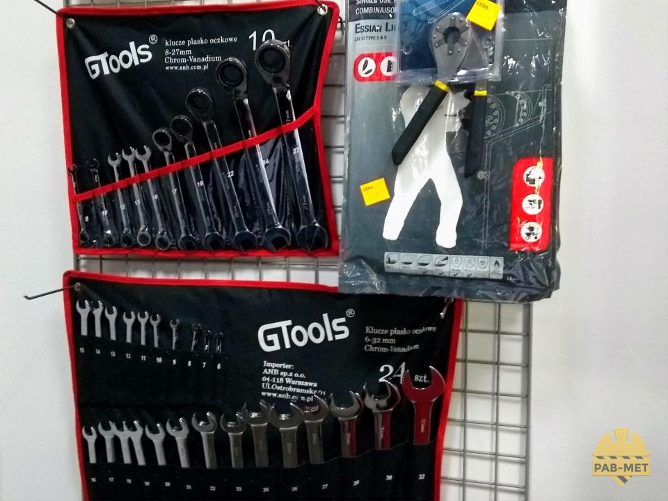 Ekspozycja w sklepie z narzędziami: dwa komplety kluczy płasko-oczkowych GTools w czarnych, zwijanych pokrowcach z czerwonymi obwódkami, oraz opakowanie klucza uniwersalnego z białą rękawicą...